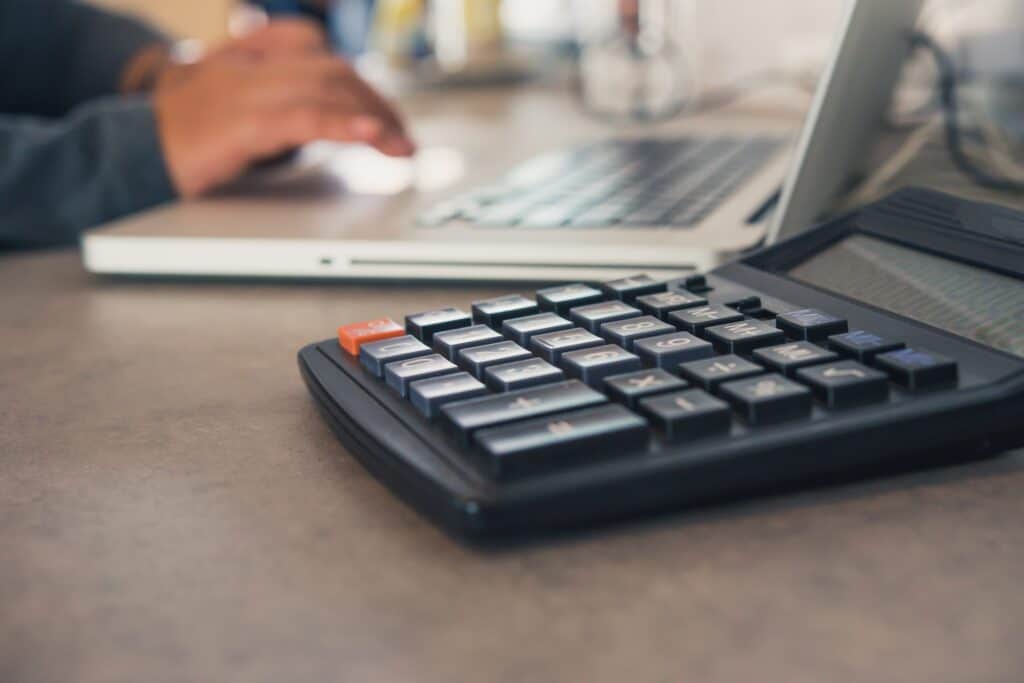A calculator beside a laptop on the table in the concept of 'how to save money when moving to East London'.