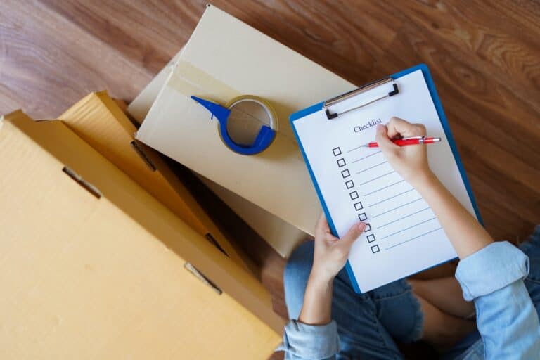 Top view of a woman holding a blank checklist on top of a stack of cardboard boxes in the concept of 'How to Create a Moving Checklist for a Stress-Free Move to East London'.