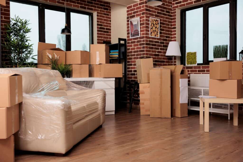 A living room filled with moving boxes and a couch wrapped in film
